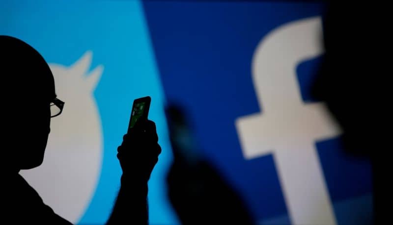 Siluetti henkilö, joka manipuloi matkapuhelinta Facebook- ja Twitter-taustalla