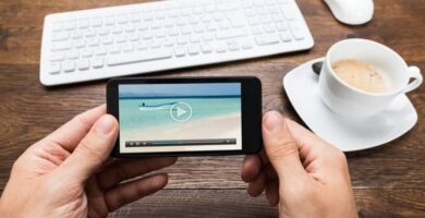 Kuinka laittaa tekstitykset videoihini Android -matkapuhelimesta? (Esimerkki) 7 manos sosteniendo movil video mar bote taza cafe teclado mouse blanco mesa madera